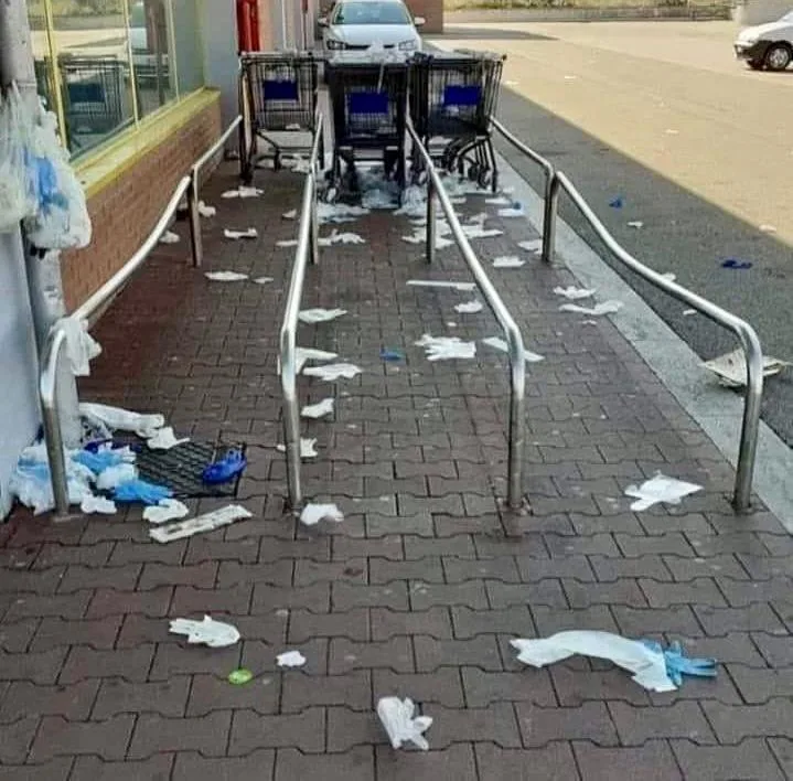 Guanti e mascherine di plastica monouso a terra davanti a un supermercato